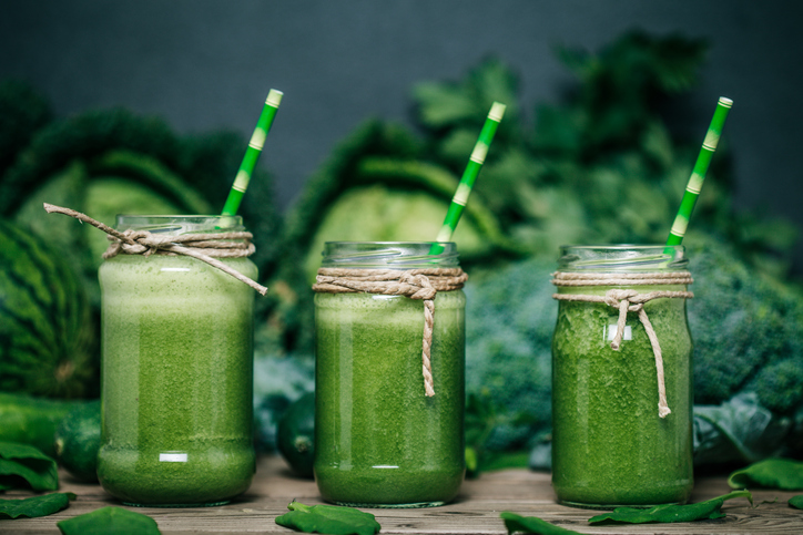 Πράσινο smoothie λαχανικών, τρία ποτήρια, λάχανο, μπρόκολο και μπιζέλια στο βάθος